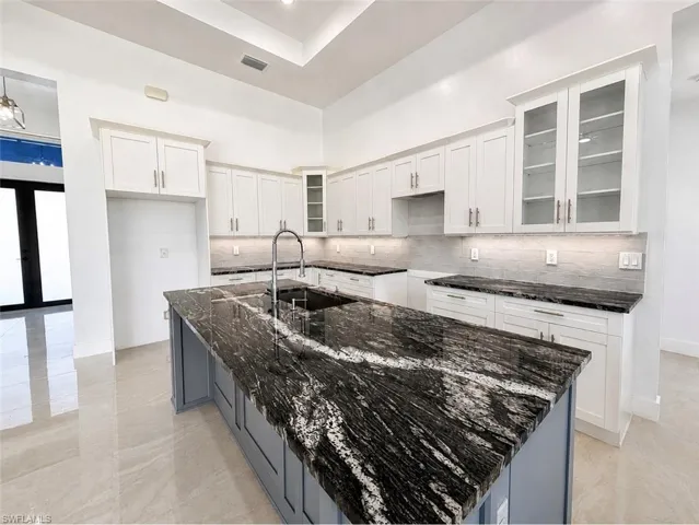 Kitchen featuring a large central island with a dramatic veined countertop, an undermount sink, and a gooseneck faucet