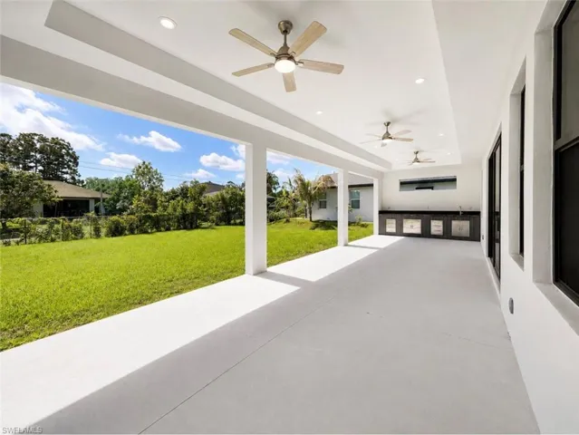Spacious covered patio with a built-in outdoor kitchen, featuring a sink, dark cabinetry, and light countertops
