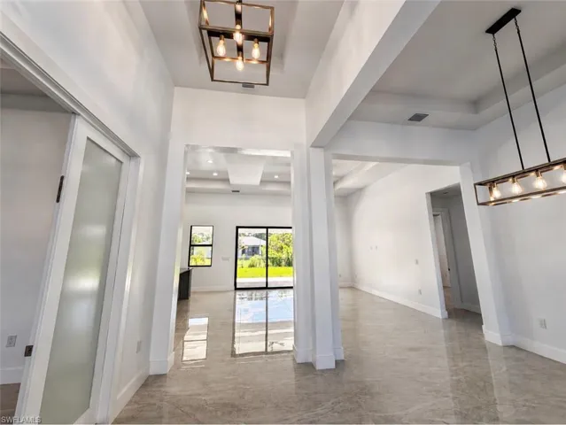 Spacious interior with polished large format tile flooring, contemporary lighting fixtures, high ceilings, tray ceiling details, and a sliding glass door leading to the exterior