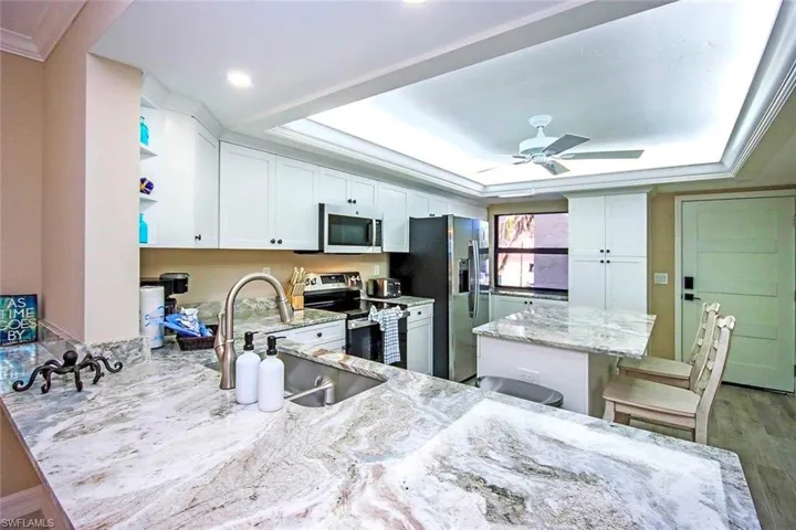 Kitchen featuring appliances with stainless steel finishes, a peninsula, light stone counters, a kitchen bar, and white cabinets
