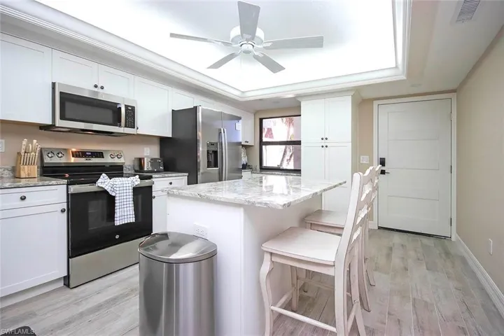 Kitchen featuring stainless steel appliances, light wood-style floors, white cabinetry, a kitchen island, and a kitchen bar