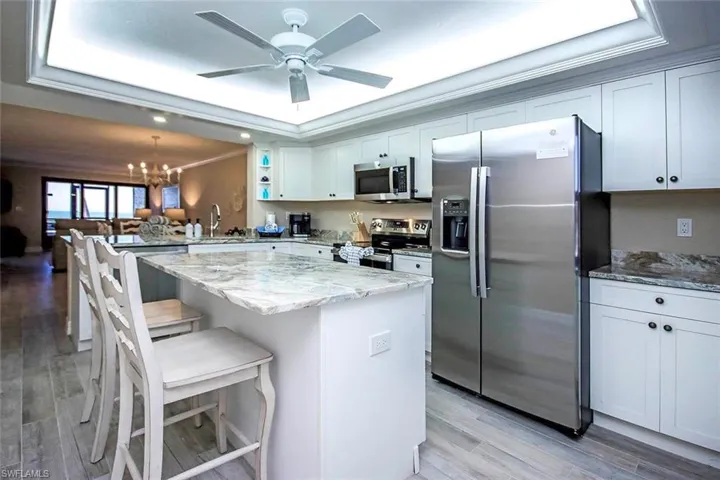 Kitchen with appliances with stainless steel finishes, a kitchen bar, light stone countertops, open shelves, and a raised ceiling