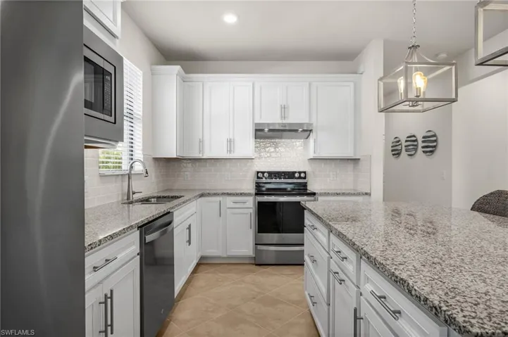 Kitchen with large Island and stainless steel appliances  white cabinetry, light stone countertops, under cabinet range hood, and pendant lighting