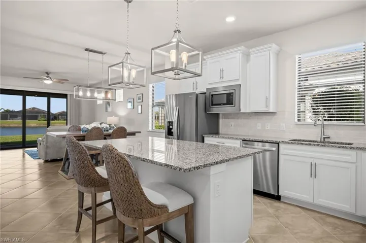 Kitchen with backsplash, a breakfast bar area, light stone counters, white cabinetry, and a kitchen island