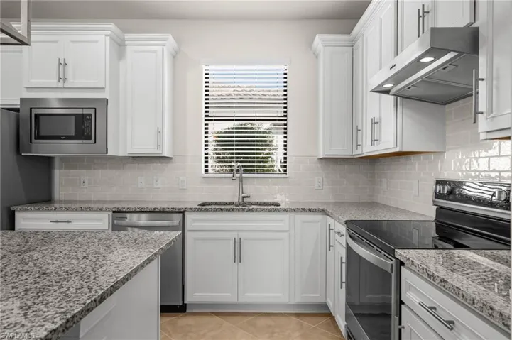 Kitchen with stainless steel appliances, extractor fan, white cabinets, and light stone countertops