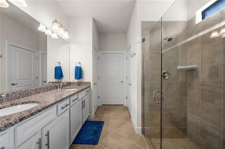 Bathroom with double vanity, a shower stall, and light tile patterned floors