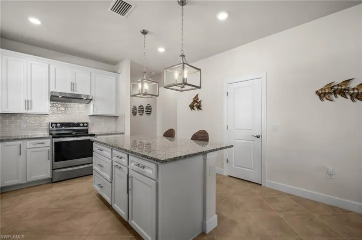 Kitchen with electric stove, decorative backsplash, decorative light fixtures, a kitchen island, and under cabinet range hood