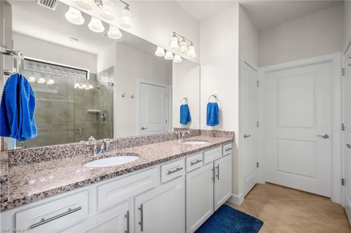 Bathroom featuring double vanity, a stall shower, and light tile patterned floors