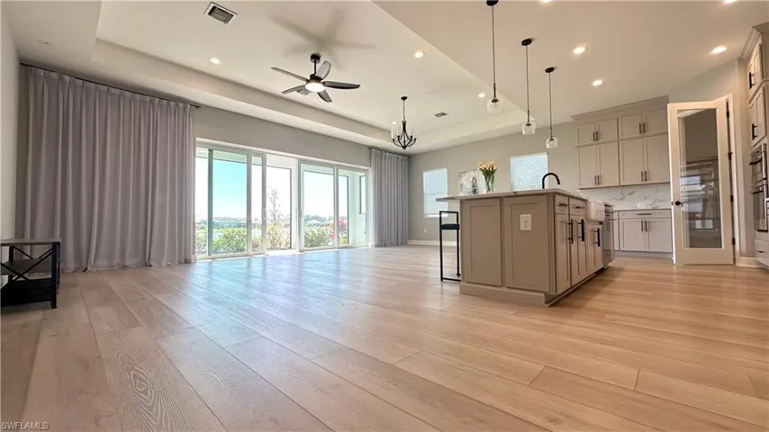 Kitchen with a kitchen bar, a raised ceiling, open floor plan, light wood-style flooring, and recessed lighting