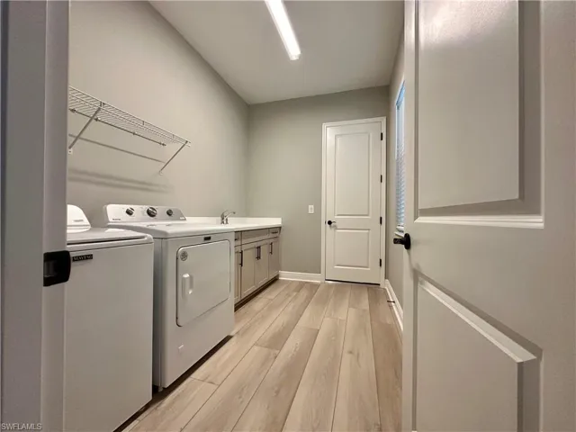 Washroom featuring washer and clothes dryer, light wood-style flooring, and cabinet space
