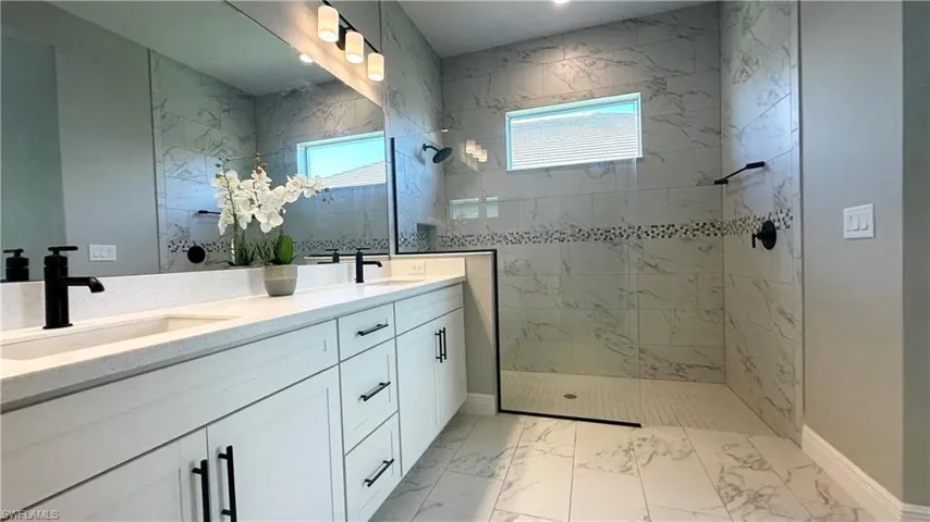 Full bath featuring double vanity, a walk in shower, and light marble finish flooring