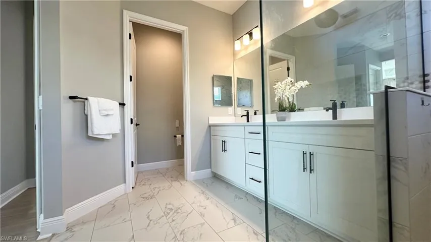 Bathroom with light marble finish floors, double vanity, and a stall shower