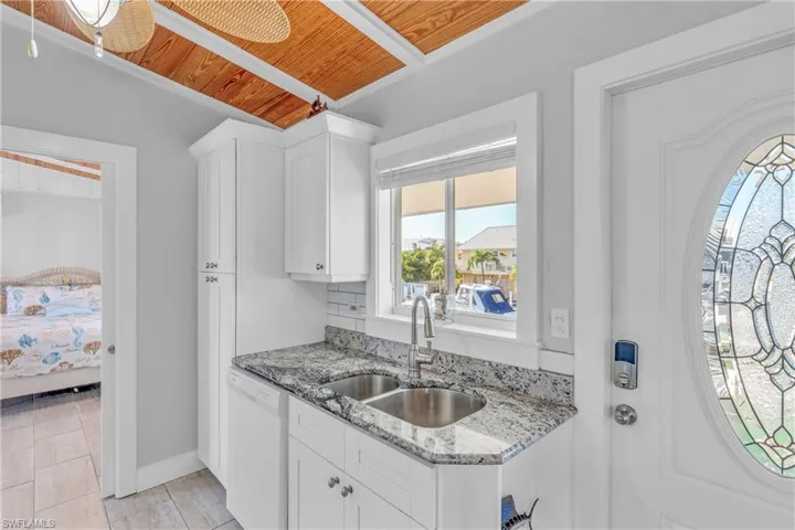 Kitchen with light stone countertops, white cabinetry, white dishwasher, and wood ceiling
