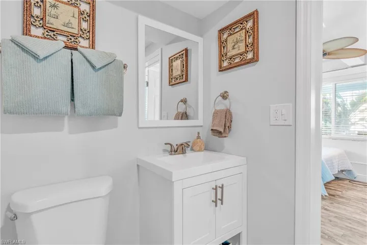 Half bath with connected bathroom, vanity, a ceiling fan, and light wood finished floors