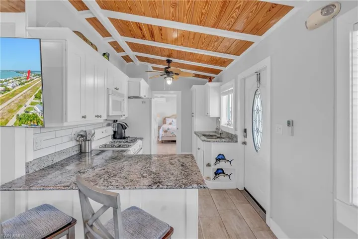 Kitchen featuring white cabinetry, a kitchen bar, a wood ceiling with exposed beams, light stone counters, and a peninsula