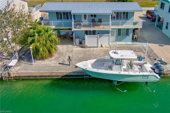 Back of house with boat lift, a metal roof, a patio, and a water view