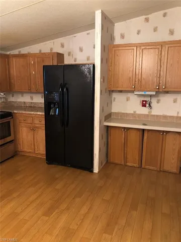 Kitchen featuring lofted ceiling, light hardwood / wood-style flooring, black refrigerator with ice dispenser, and stainless steel stove