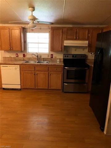 Kitchen featuring sink, black refrigerator, hardwood / wood-style flooring, electric range, and white dishwasher