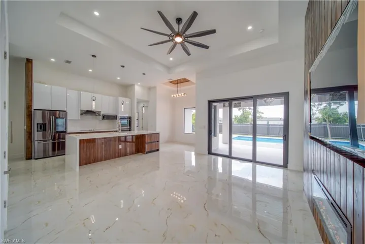 Kitchen with appliances with stainless steel finishes, white cabinets, hanging light fixtures, a large island, and a raised ceiling