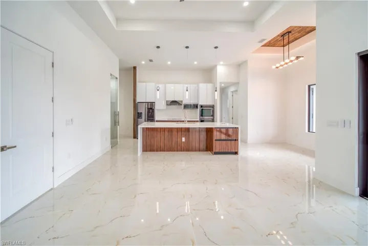 Kitchen featuring a large island, hanging light fixtures, a raised ceiling, and white cabinets