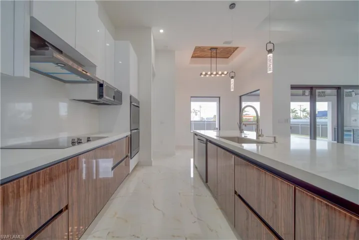 Kitchen featuring sink, decorative light fixtures, appliances with stainless steel finishes, a tray ceiling, and white cabinets