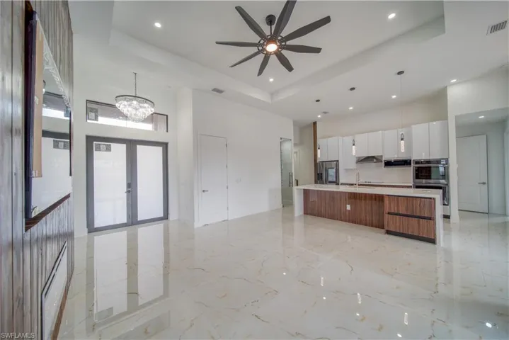 Kitchen with decorative light fixtures, a large island with sink, a raised ceiling, and white cabinets
