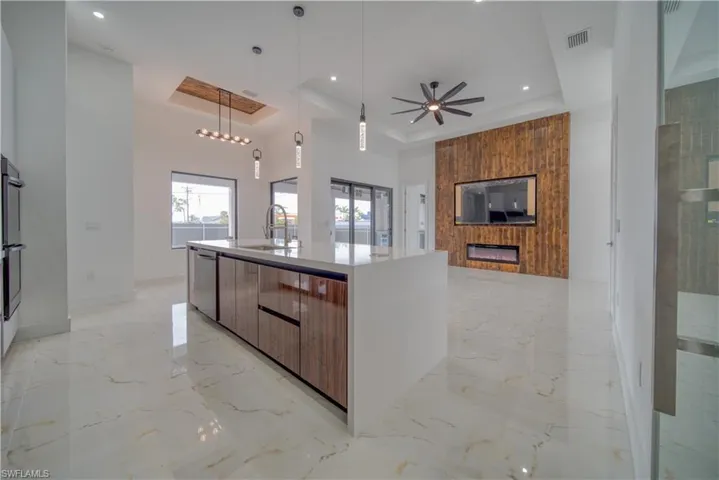Kitchen featuring decorative light fixtures, a center island with sink, a large fireplace, and a tray ceiling