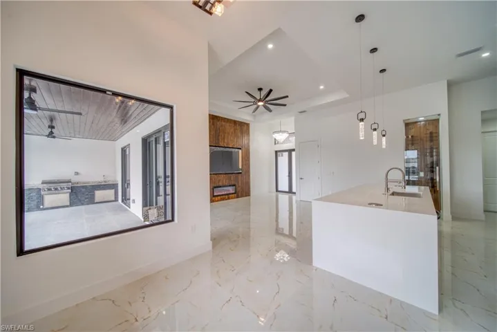 Kitchen with sink, a fireplace, an island with sink, decorative light fixtures, and a raised ceiling