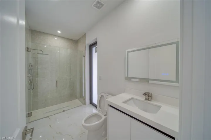 Bathroom featuring a shower with door, vanity, and toilet