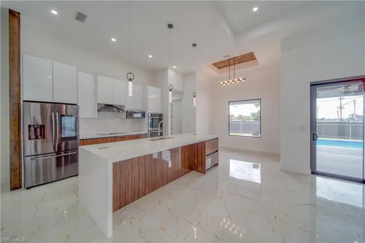 Kitchen featuring decorative light fixtures, sink, white cabinets, a kitchen island with sink, and stainless steel appliances