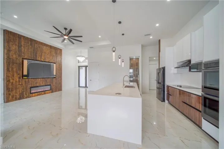 Kitchen featuring stainless steel appliances, extractor fan, white cabinets, a center island with sink, and decorative light fixtures