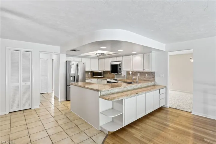 Kitchen with light hardwood / wood-style floors, kitchen peninsula, backsplash, white cabinetry, and appliances with stainless steel finishes