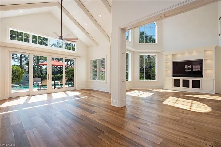 Living room featuring sliding doors, high vaulted ceiling, hardwood floors, a ceiling fan, and beam ceiling
