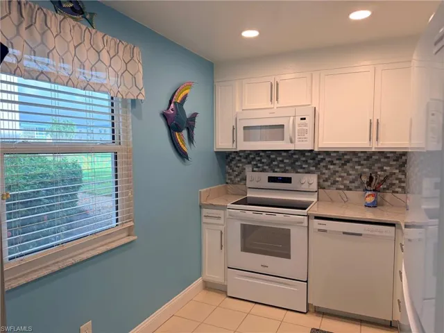 Kitchen featuring white cabinetry, solid-surface countertops, multi-toned mosaic tile backsplash, built-in appliances, and tile flooring
