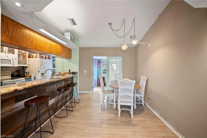 Kitchen featuring a kitchen bar, light stone counters, white appliances, and light hardwood / wood-style flooring