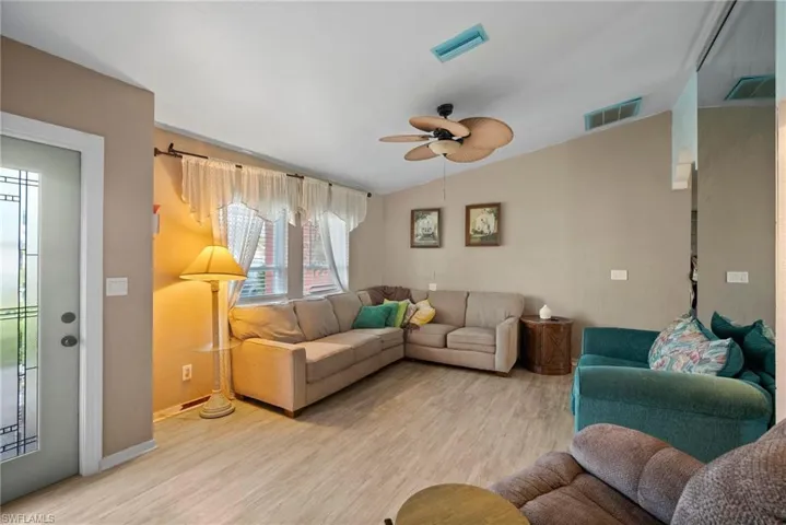 Living room with ceiling fan, light wood-type flooring, and vaulted ceiling