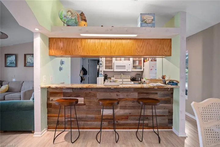 Kitchen with a kitchen bar, lofted ceiling, white appliances, and light wood-type flooring