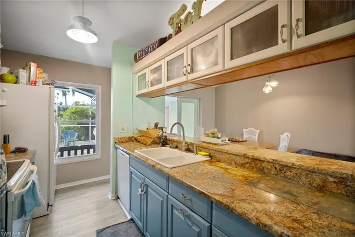 Kitchen with white appliances, blue cabinets, sink, light stone countertops, and light wood-type flooring