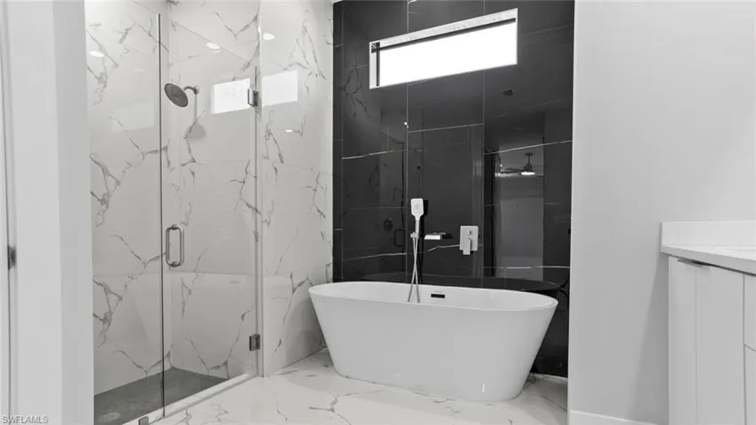 Bathroom with marble finish floor, a marble finish shower, vanity, and a soaking tub