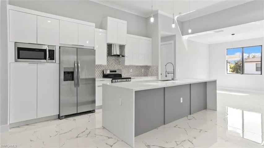 Kitchen featuring stainless steel appliances, white cabinetry, marble finish floor, wall chimney exhaust hood, and crown molding