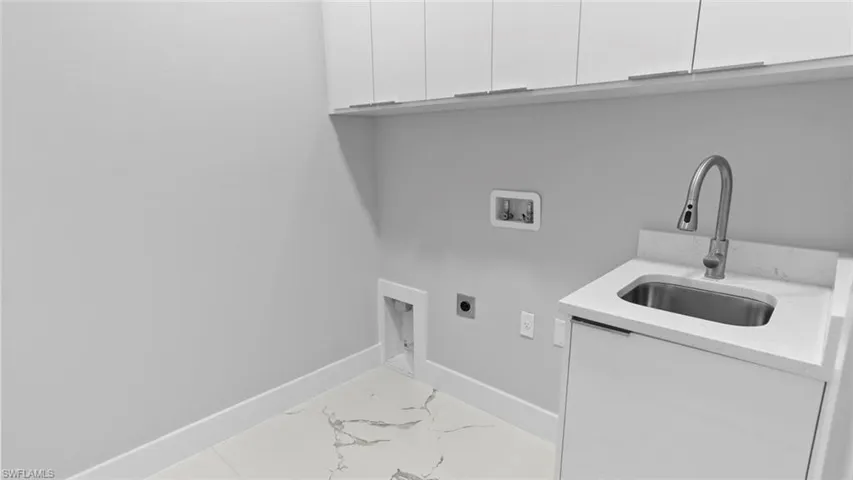 Washroom with hookup for a washing machine, hookup for an electric dryer, a sink, baseboards, and cabinet space