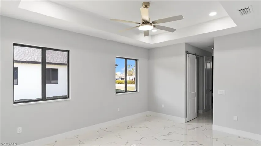 Spare room with a barn door, visible vents, baseboards, marble finish floor, and a raised ceiling