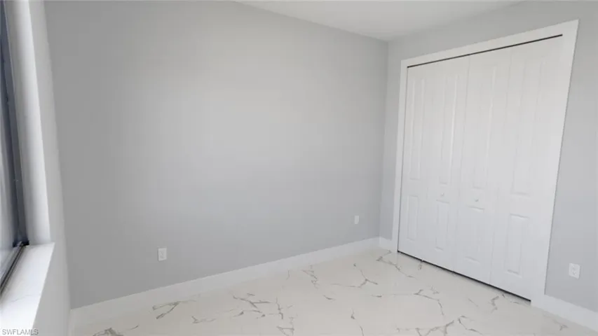 Unfurnished bedroom featuring marble finish floor, a closet, and baseboards