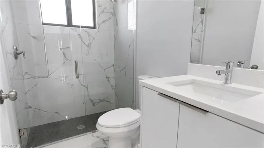 Full bath with a marble finish shower, marble finish floor, vanity, and toilet