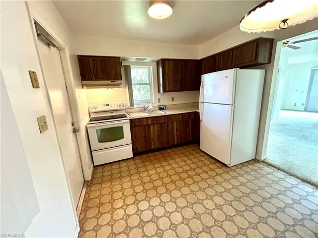 Kitchen featuring light tile patterned floors, dark brown cabinetry, and white appliances