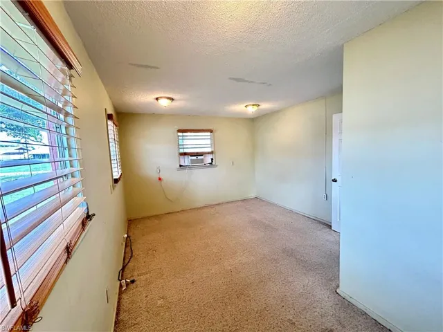 Empty room with a textured ceiling, carpet, and cooling unit