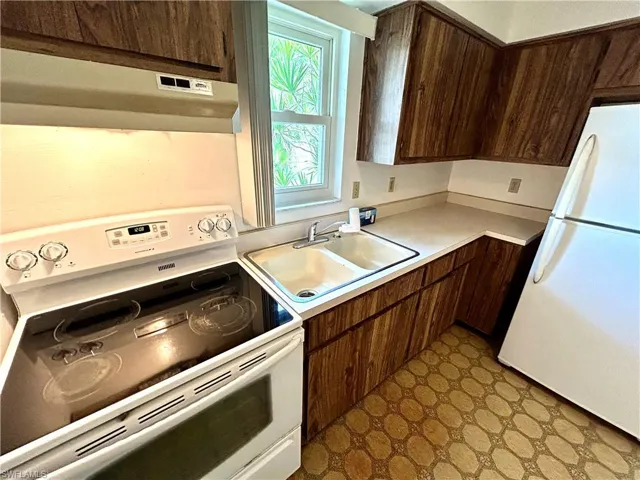 Kitchen featuring dark brown cabinetry, sink, white appliances, light tile patterned flooring, and range hood