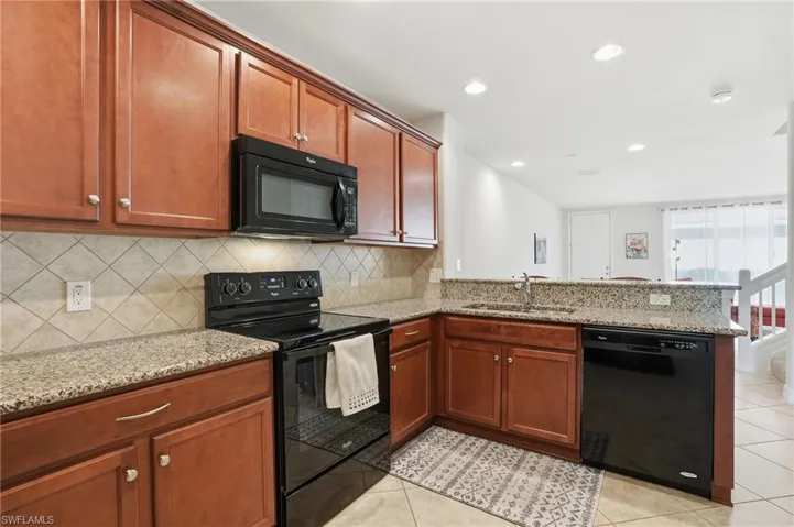 Kitchen featuring black appliances, a peninsula, light stone countertops, light tile patterned flooring, and recessed lighting