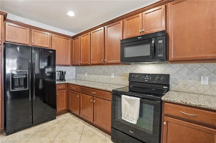 Kitchen with black appliances, wood finish cabinetry, light stone countertops, light tile patterned floors, and recessed lighting