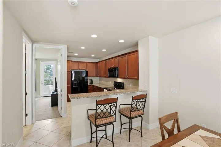 Kitchen with a kitchen breakfast bar, black appliances, light stone counters, a peninsula, and recessed lighting